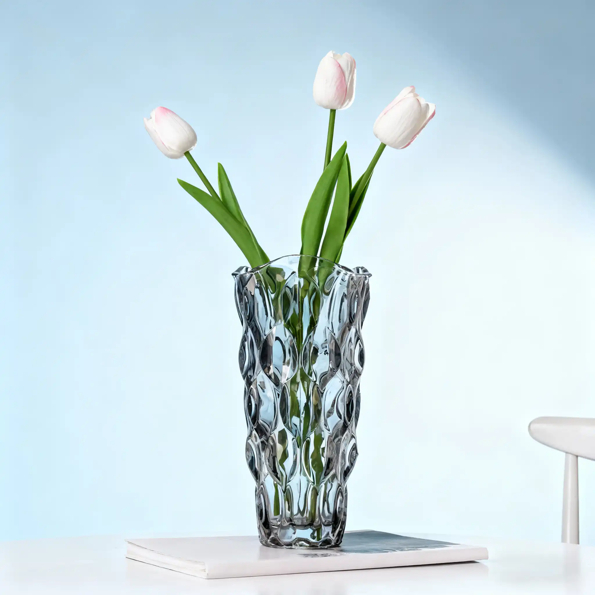Grey textured glass vase with white and pink tulips, placed on a book against a light blue background.